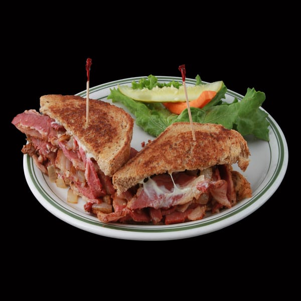 A Golden Ox Brundage American deli sandwich with meat, cheese, and onions, served with a pickle and lettuce.
