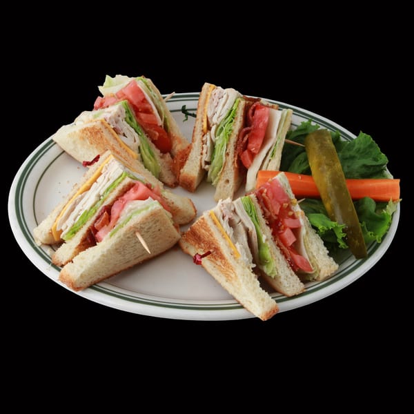 A plate of Golden Ox Brundage club sandwiches with turkey, bacon, lettuce, tomato, and cheese.