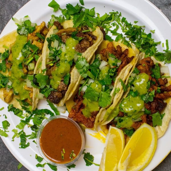 A plate of Golden Ox Brundage tacos with green sauce, cilantro, onions, and lemon wedges.