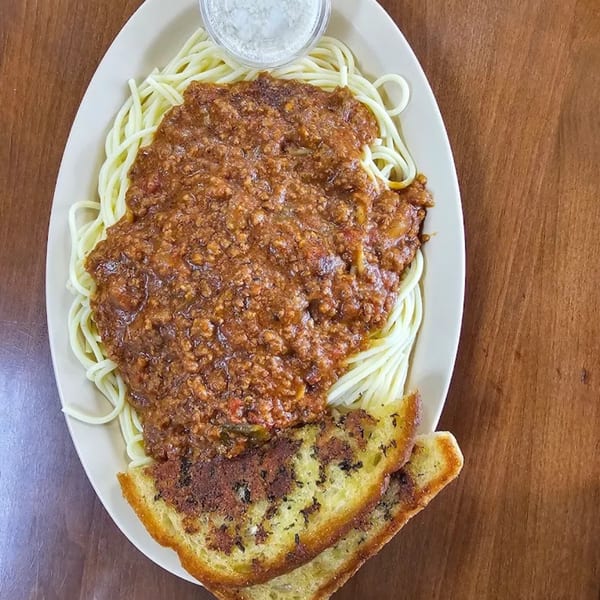 Spaghetti with meat sauce, two slices of garlic bread, and a small cup of parmesan cheese.